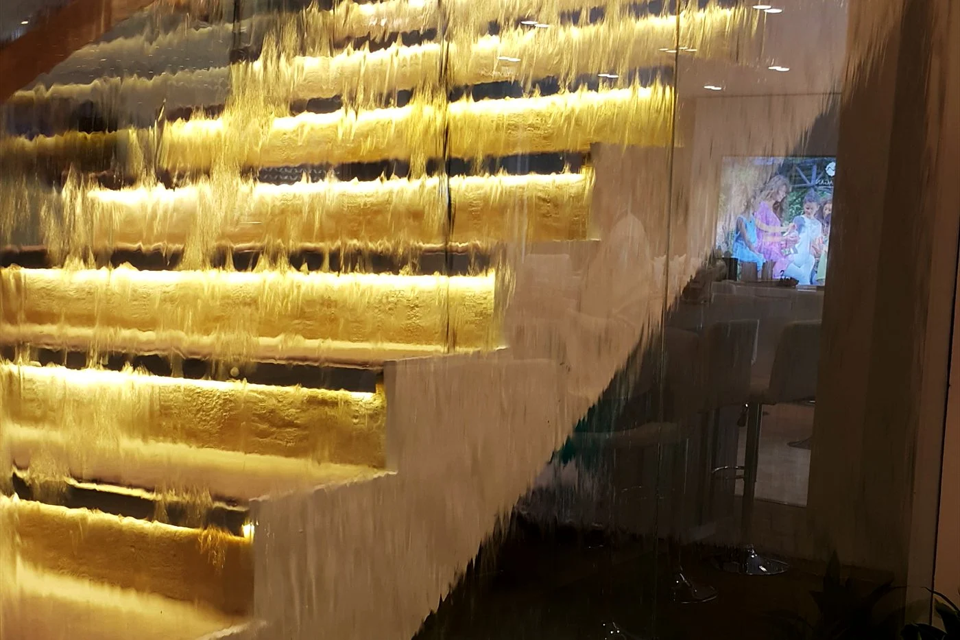 Backlit glass staircase with water cascading behind it